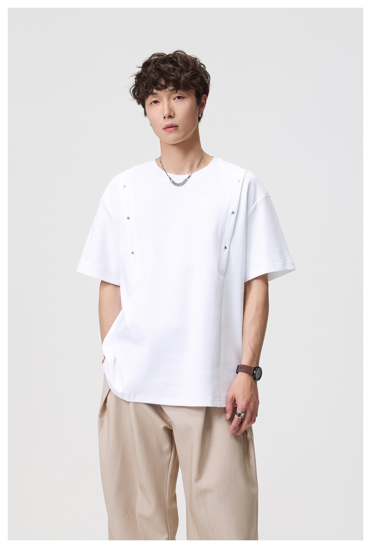 Model wearing a white oversized crew-neck tee with short sleeves and snap-fastened front straps, shown from the front.