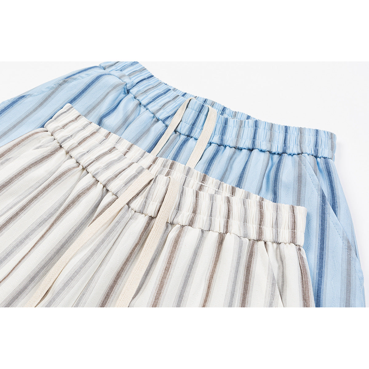 Close-up of overlapping elastic waistbands on blue and cream striped pants, with cream drawstrings.
