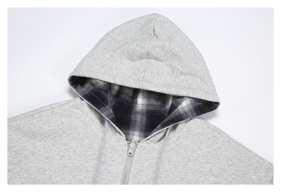 Close-up of a light gray hoodie showing its plaid-lined hood, gray drawstrings, and front zipper.