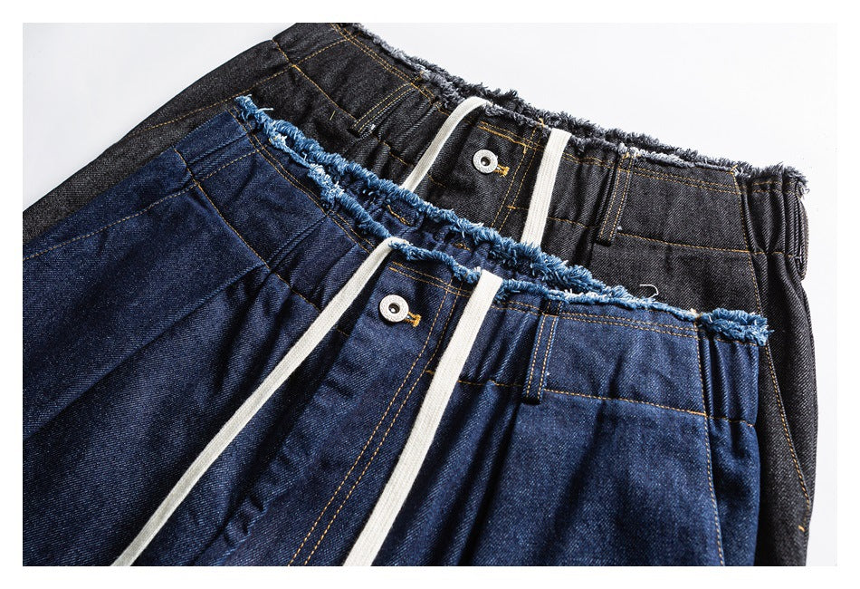 Close-up of indigo and charcoal jeans showing frayed elastic waistbands, drawstrings, and metal buttons.