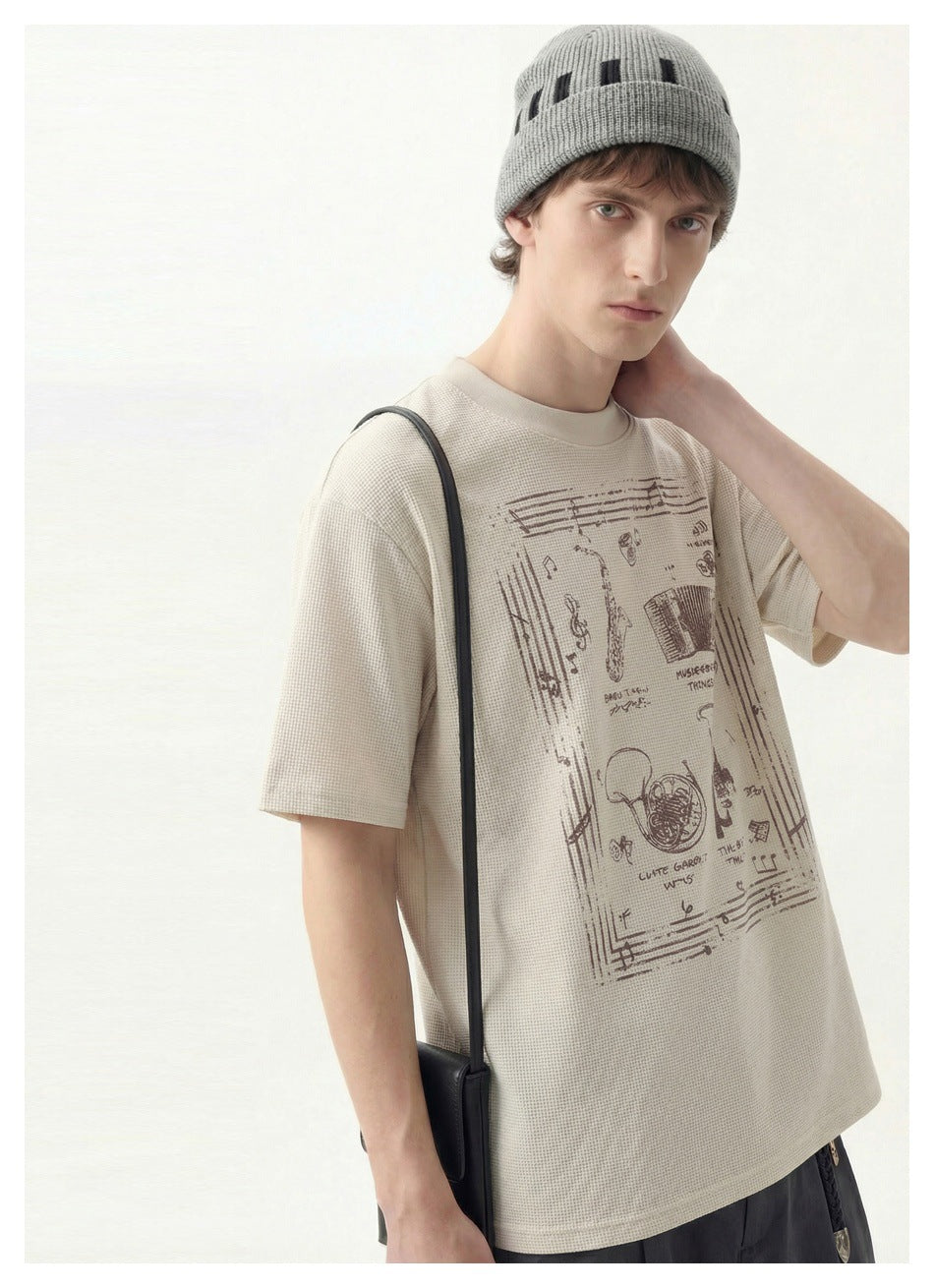 Close view of a model wearing an ivory music-graphic T-shirt and gray beanie.