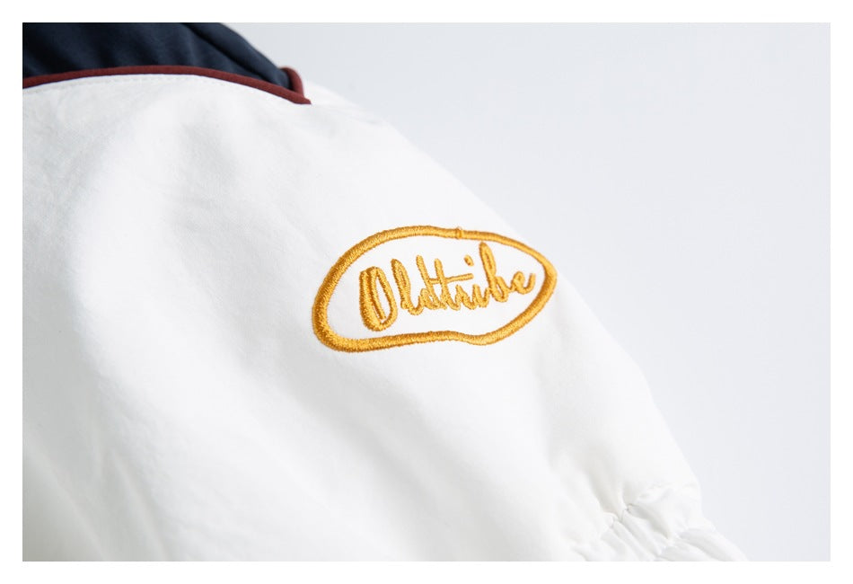 White garment detail with a gold embroidered oval script emblem and dark navy fabric edged in red.