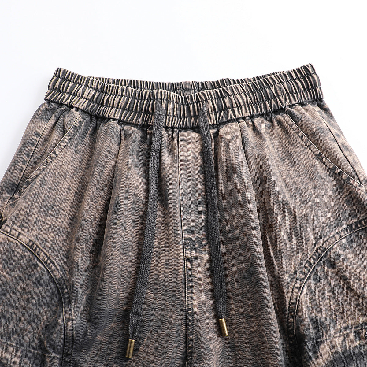 Close front view of brown-gray patterned pants with a gathered elastic waist, black drawstrings, and curved panel seams.
