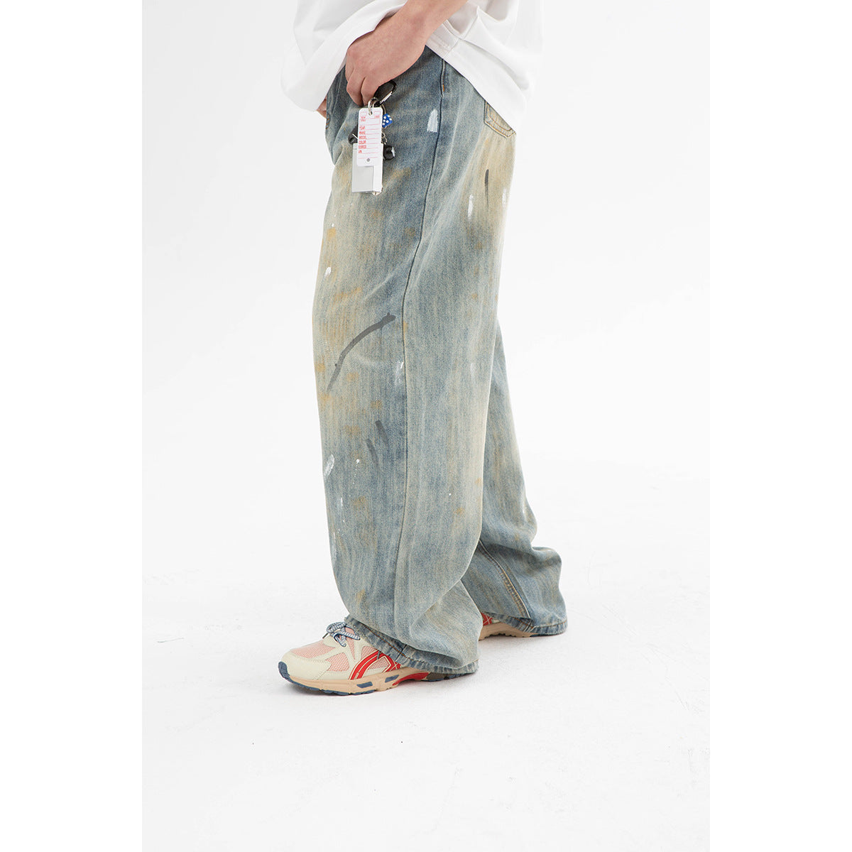 Close side view of very wide faded blue jeans with distressed paint-like marks and a small hanging tag.
