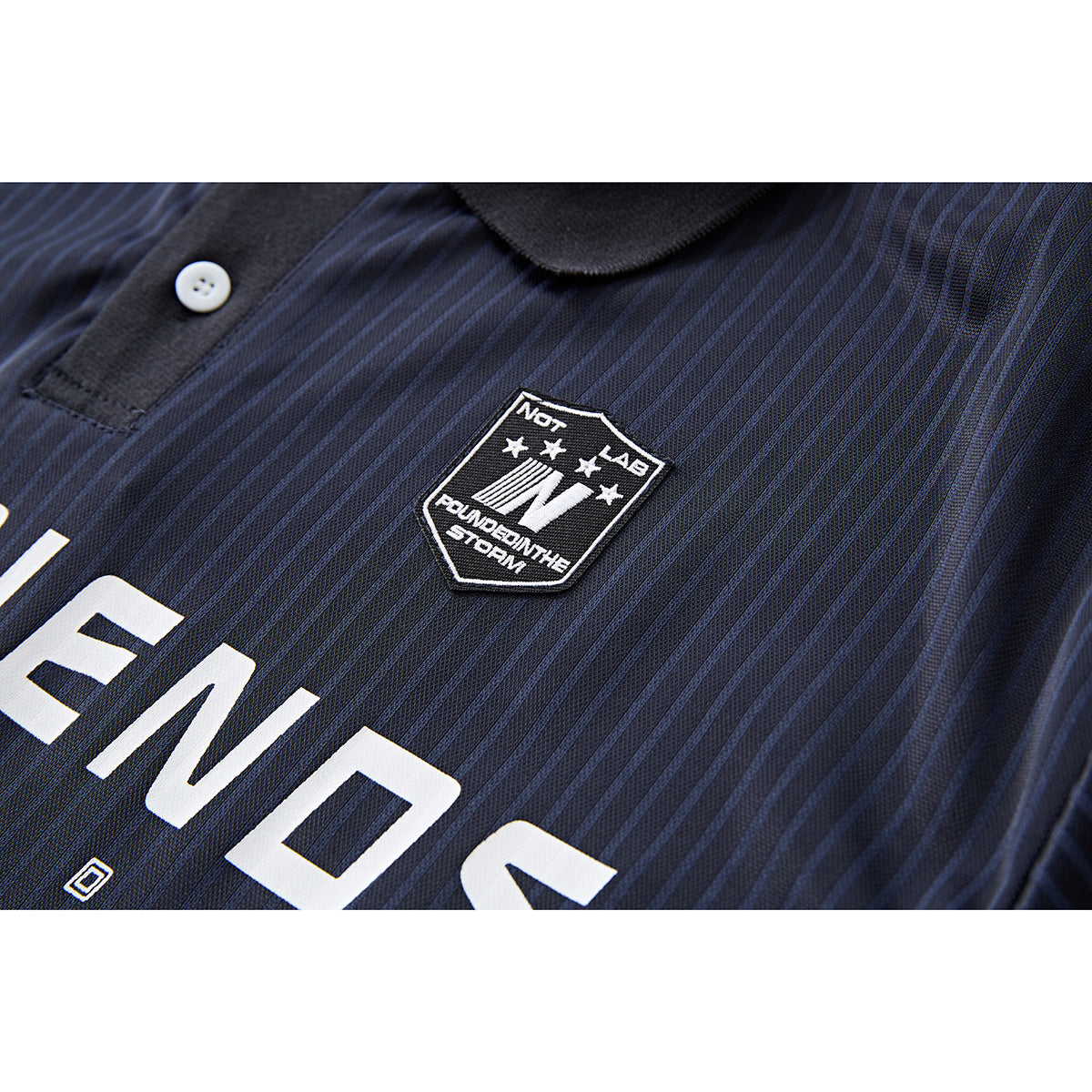 Close-up of a navy pinstriped polo shirt’s chest patch and large white lettering.