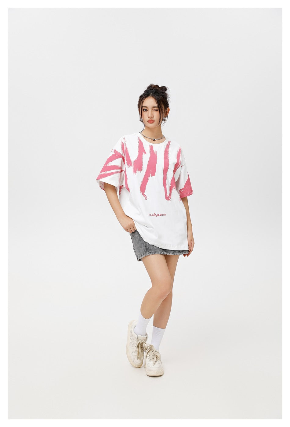 Model wearing white oversized T-shirt with pink brushstroke print and a gray denim mini skirt, full-length pose