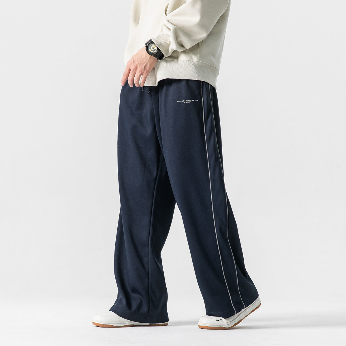 Model wearing navy wide-leg pants with thin light piping and small text on the thigh, shown from the side.