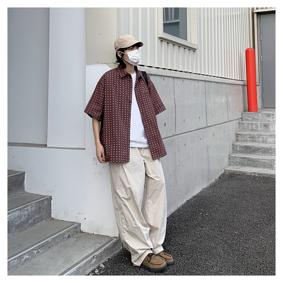Person wearing a burgundy patterned short-sleeve button-up shirt over a white tee with loose beige trousers.