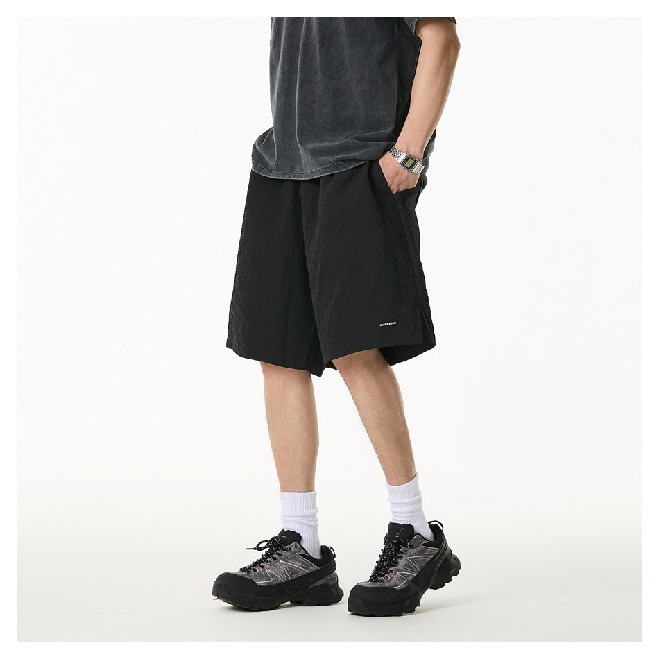 Angled view of a model wearing loose black knee-length shorts with a small white hem label.