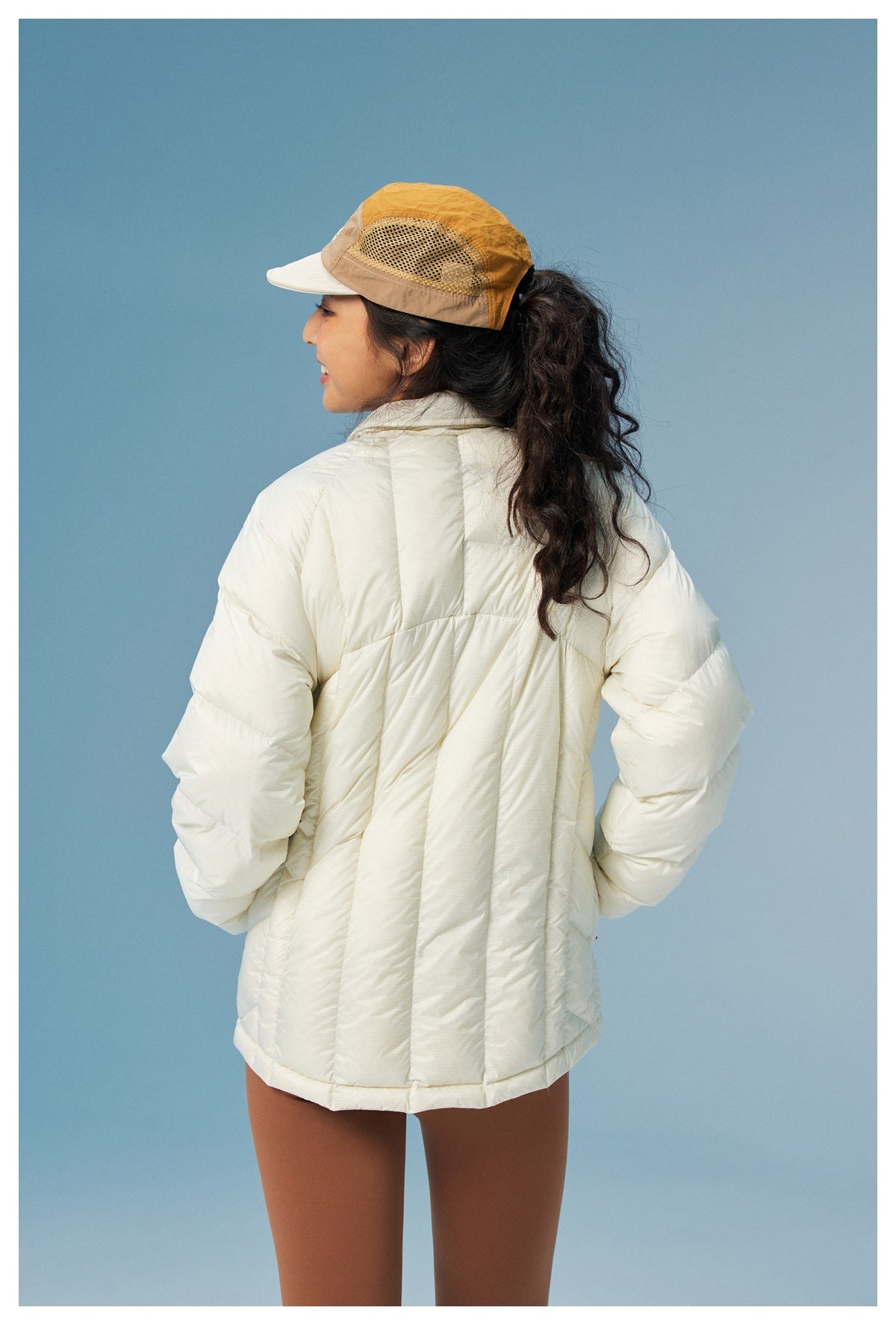 Rear view of a model wearing an ivory quilted jacket with paneled stitching and long sleeves.