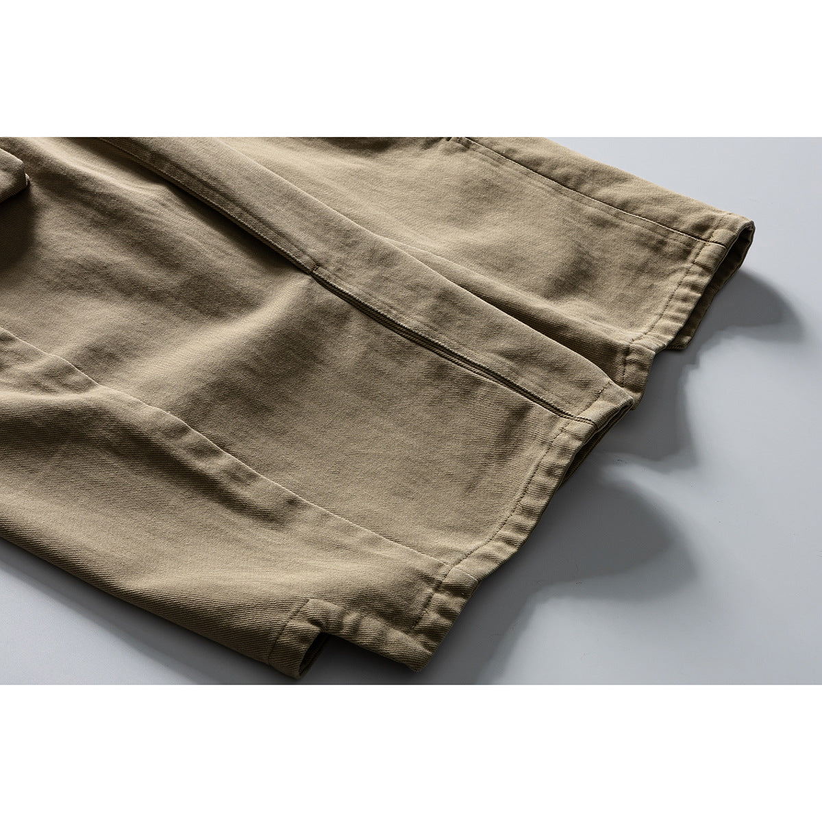 Close-up of the khaki trousers’ wide leg hems and stitched seams.