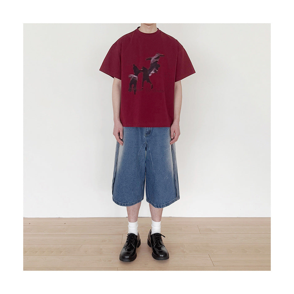 Model wearing faded blue wide-leg knee-length denim shorts with a red graphic tee and black shoes, full-length front view