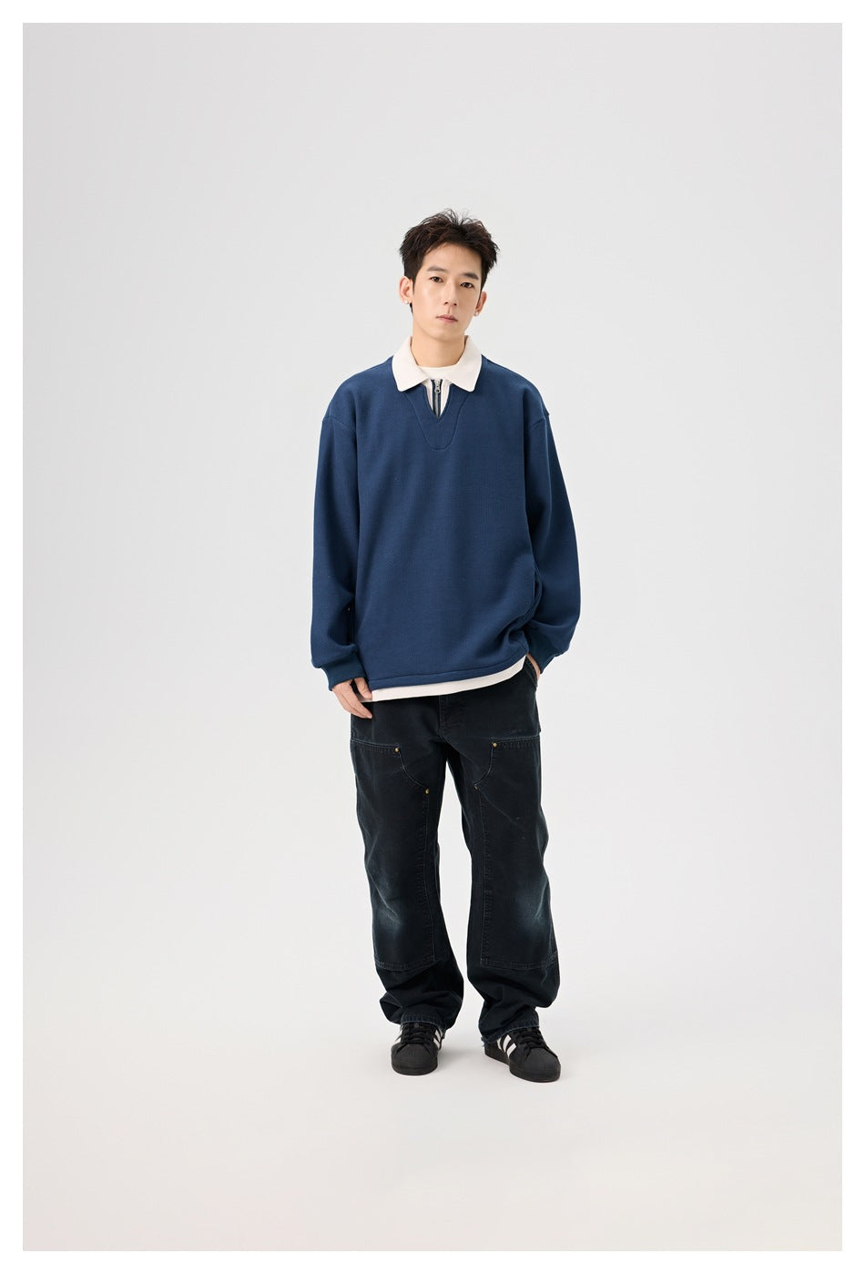 Model wearing navy polo-collar quarter-zip sweatshirt with one hand in pocket, styled with dark workwear jeans