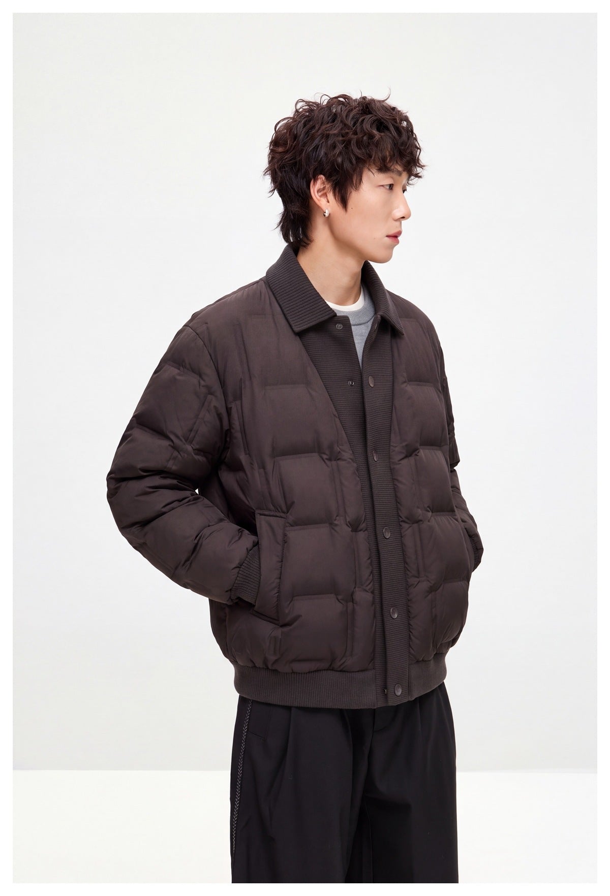 Angled view of a model wearing a dark brown quilted jacket with a ribbed collar, snap front, and patch pockets.