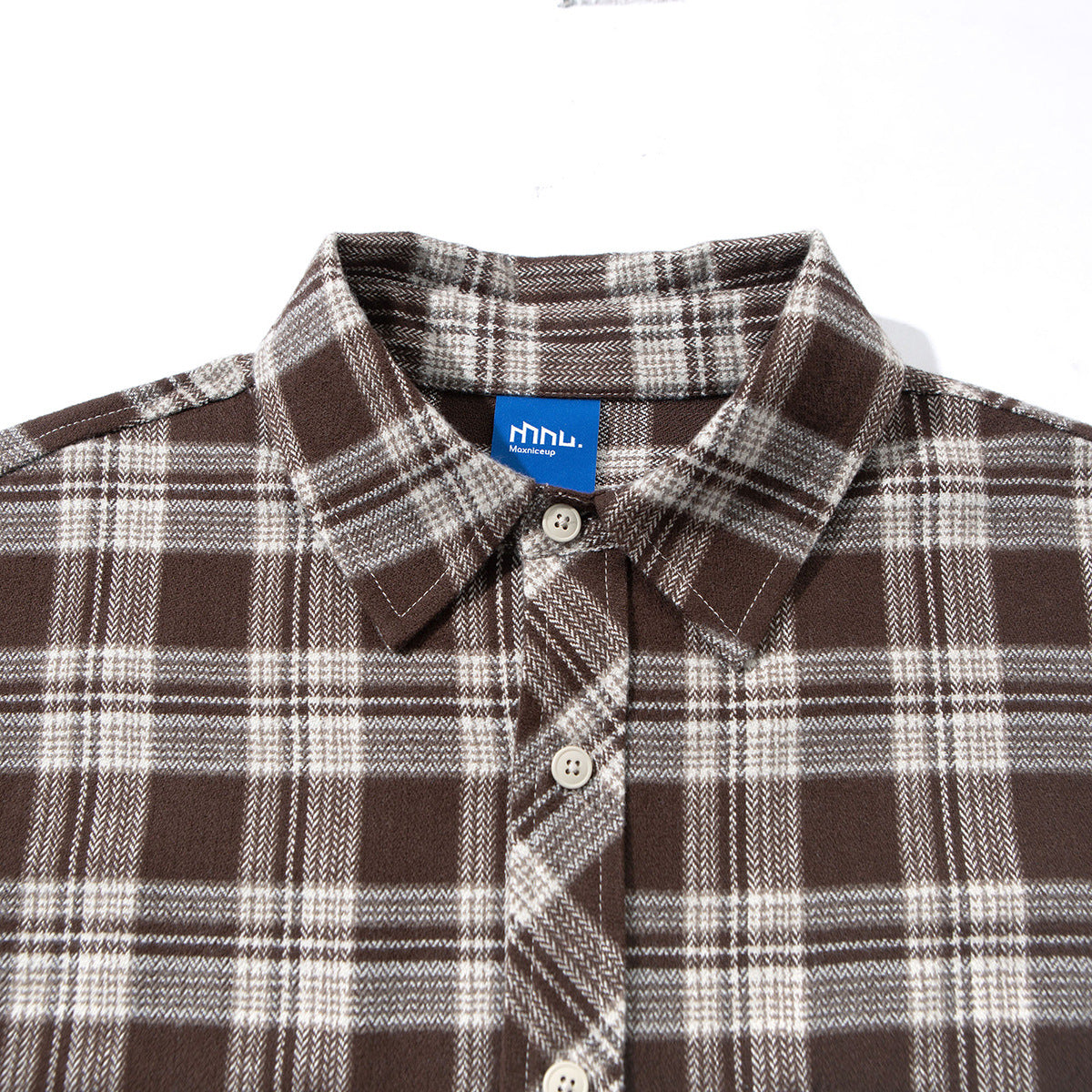 Close-up of a brown and cream plaid shirt collar, button placket, and blue neck label.
