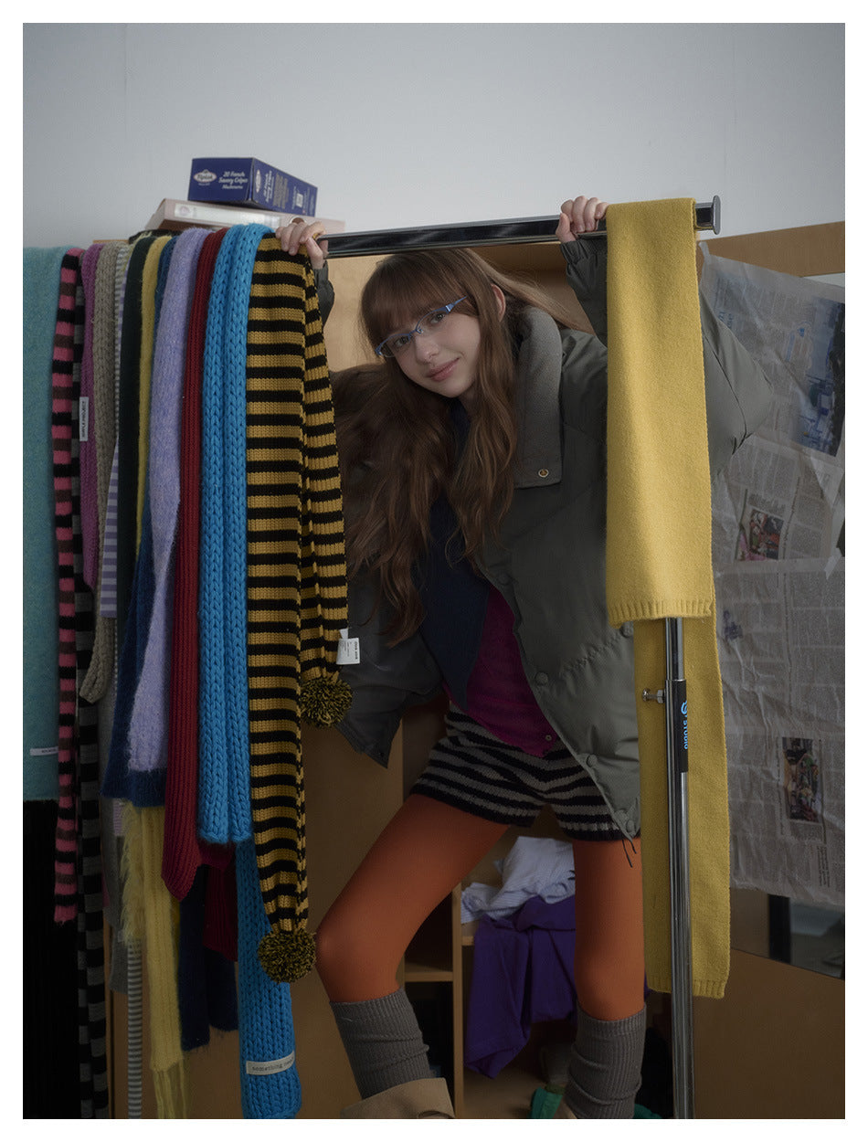 Model in a charcoal-gray puffer jacket, partly obscured by a rack of colorful scarves.