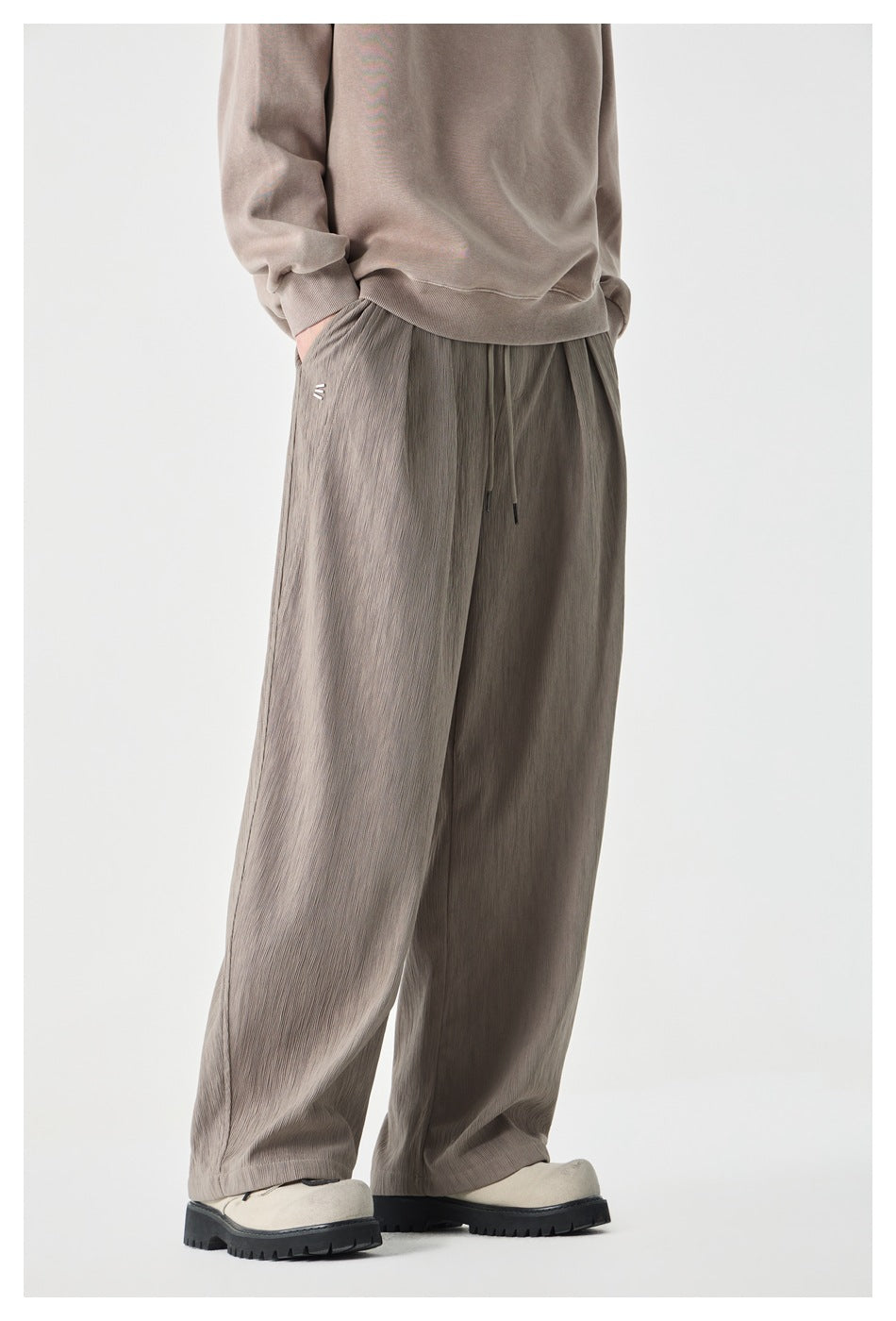 Angled side view of a model wearing taupe-gray wide-leg drawstring pants with a small hip detail.
