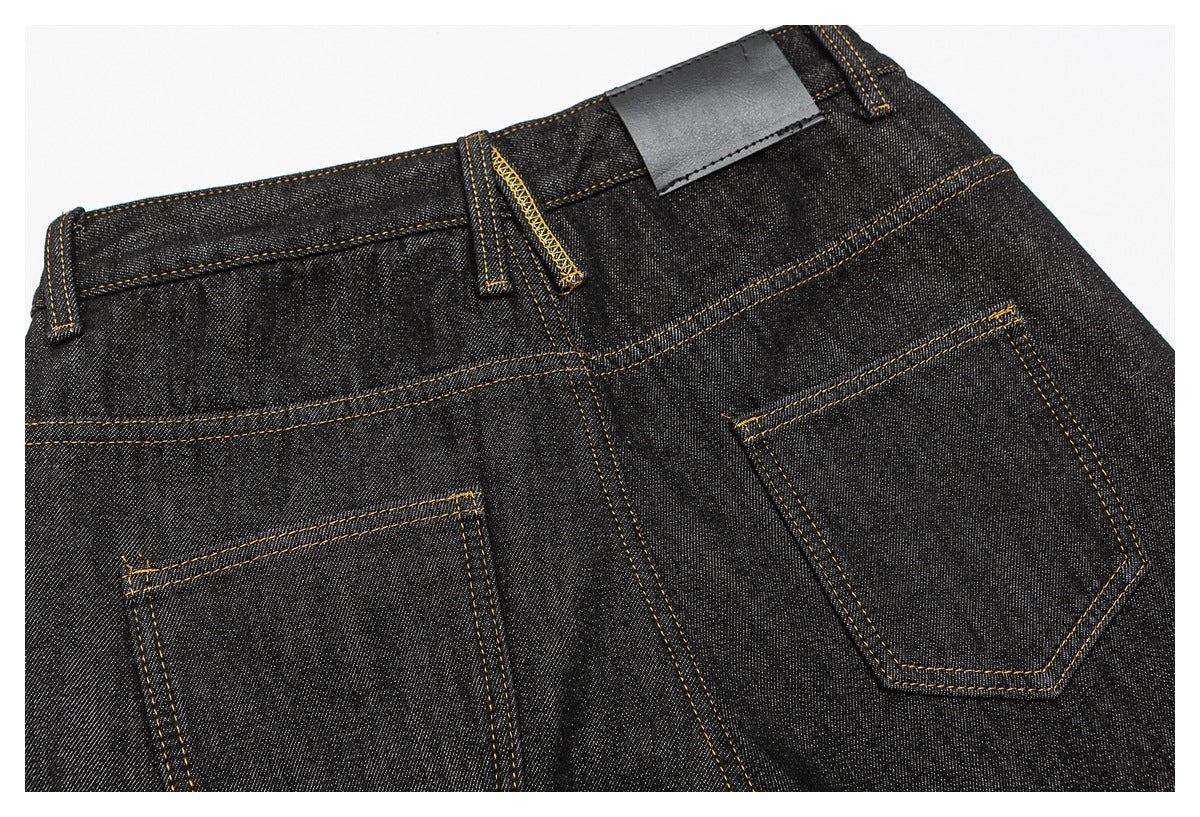 Close-up of the back waist and two pockets of black jeans with golden-brown stitching and a blank dark patch.