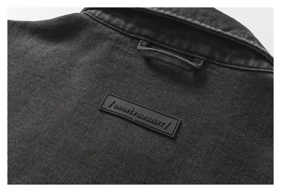 Close-up of the upper back of a black denim jacket, showing the collar, hanger loop, and a small raised label.