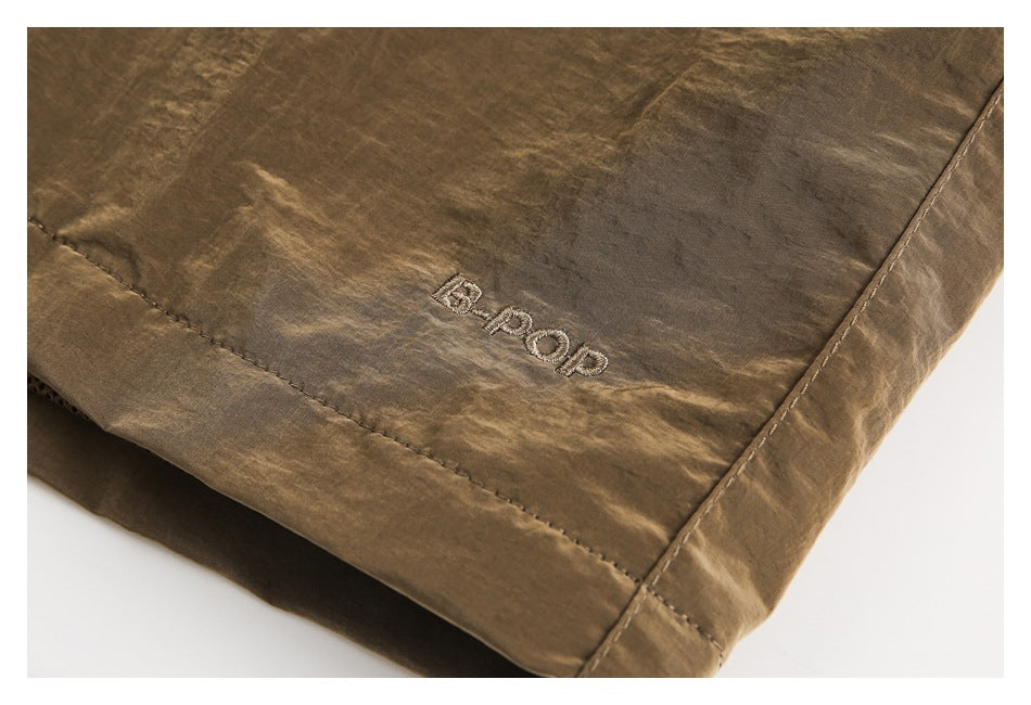 Close-up of brown shorts with a small embroidered logo near the hem.