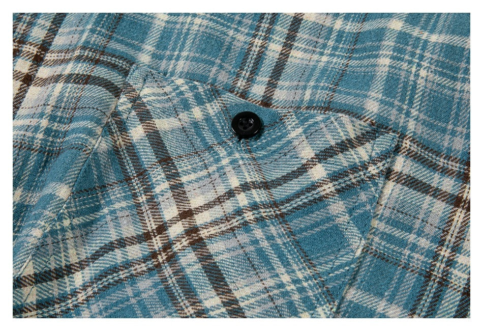 Close-up of the buttoned chest pocket and plaid pattern on a blue, cream, and brown shirt.