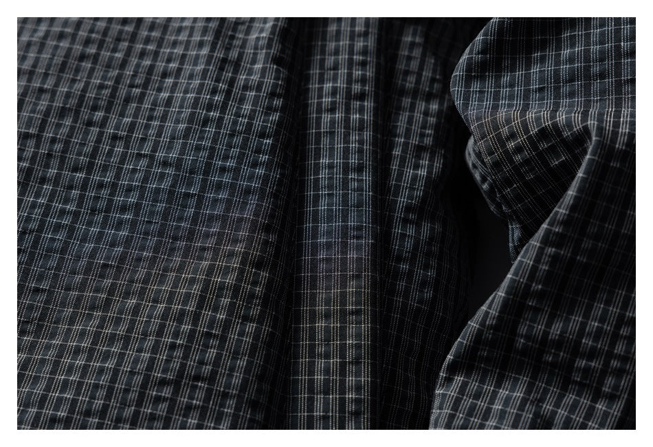 Close-up of charcoal plaid garment fabric with stitched panel seams and folds.