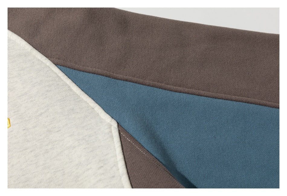 Close-up of off-white, blue, and dark brown sweatshirt fabric panels and seams.