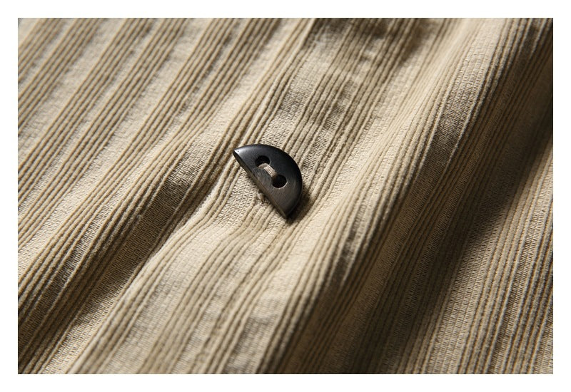 Close-up of a dark button on the tan shirt's vertically textured fabric.