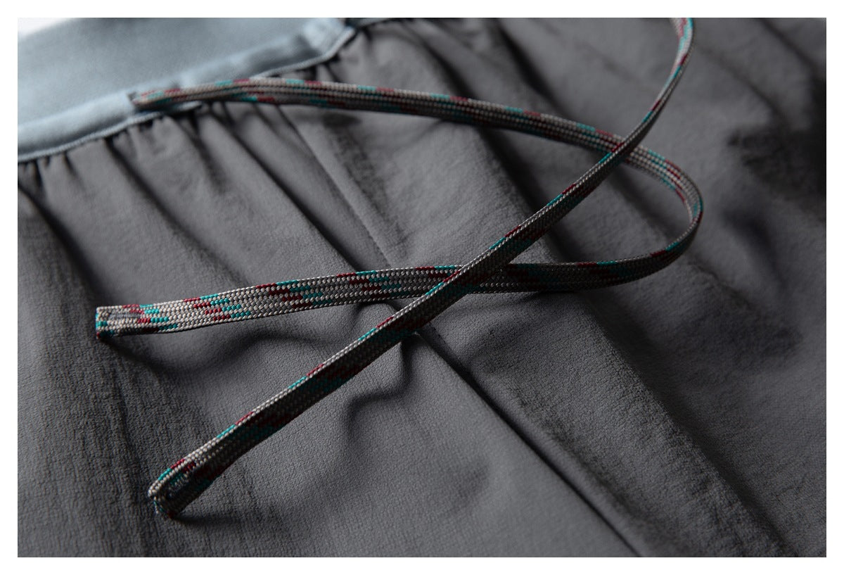 Close-up of a dark charcoal garment with a multicolored braided drawcord and light gray-blue waistband trim.