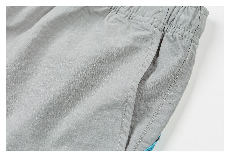 Close-up of light gray shorts showing a stitched side pocket and elastic waistband.