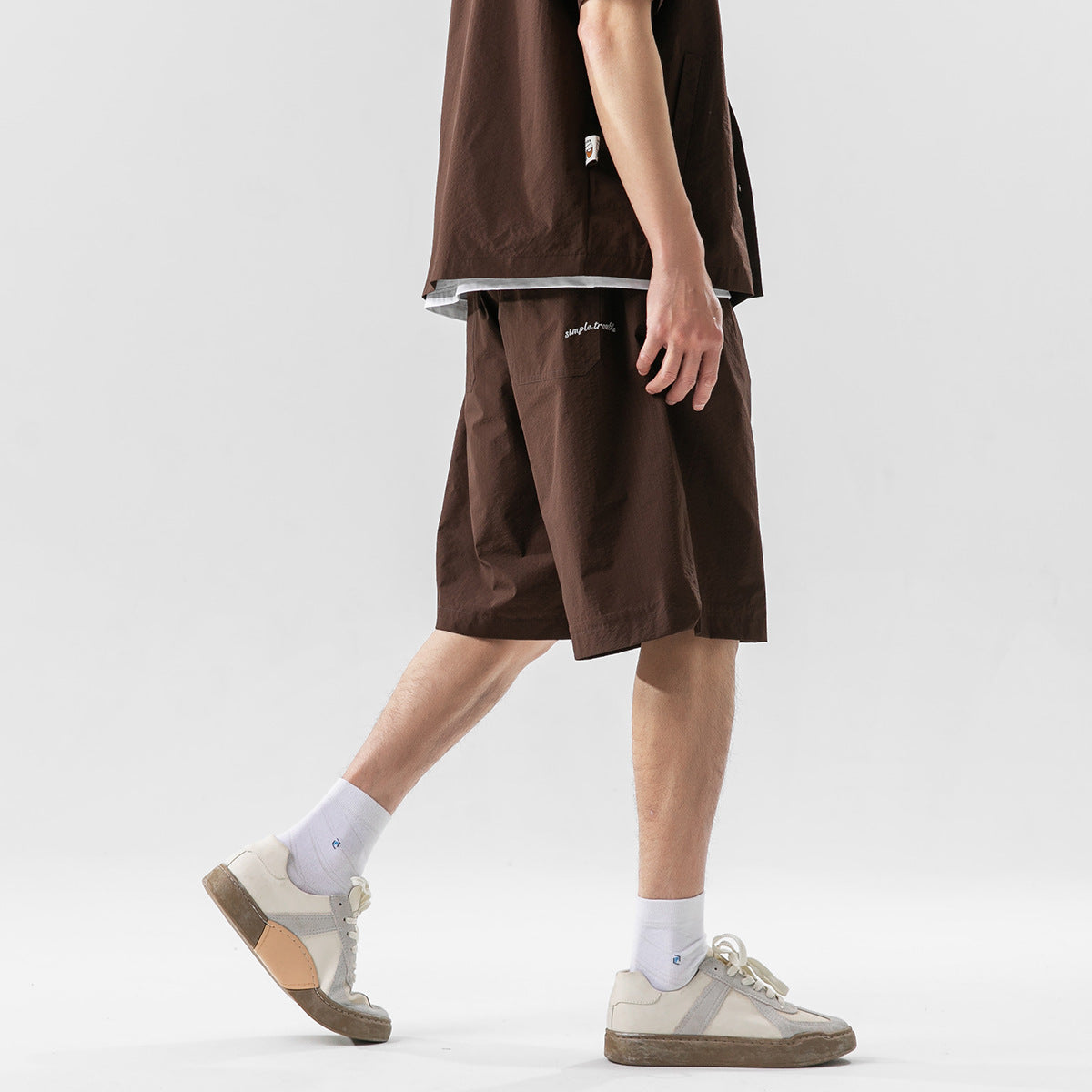 Side view of a model wearing dark brown shorts with a small white embroidered script detail.