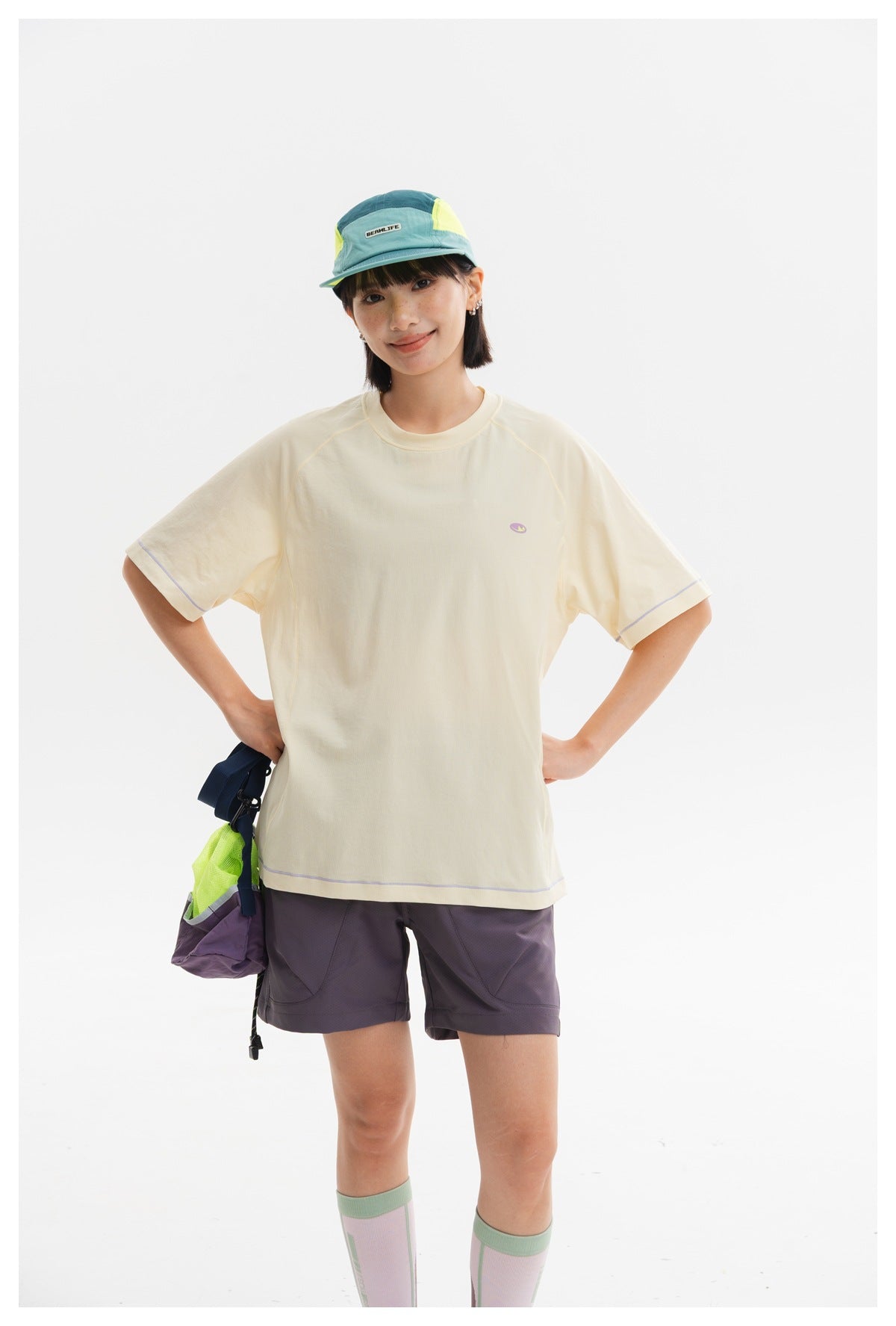 Front view of a model wearing a cream oversized T-shirt with raglan seams, lilac trim, and a small chest emblem.