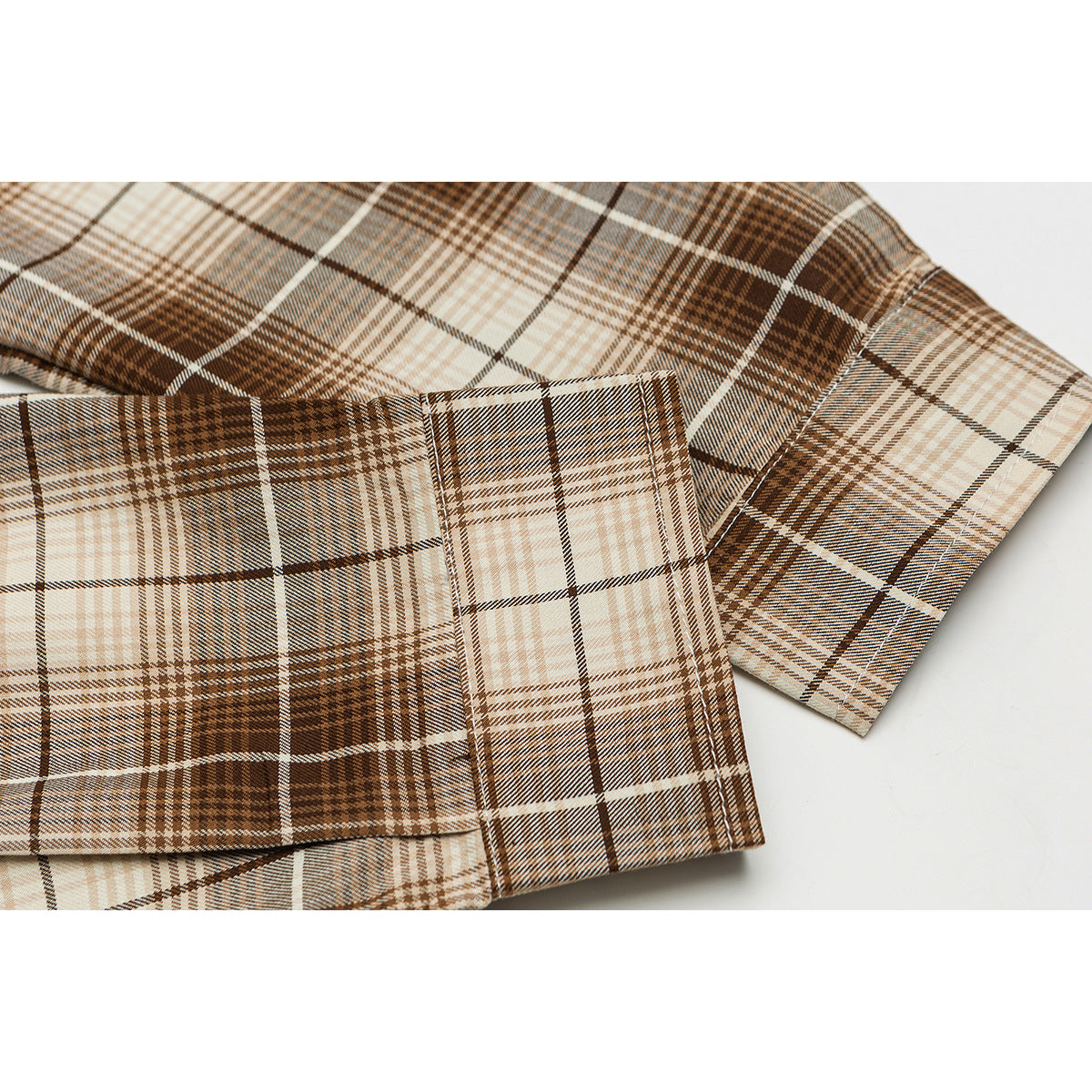 Close-up of a brown, tan and cream plaid shirt sleeve and buttoned cuff.