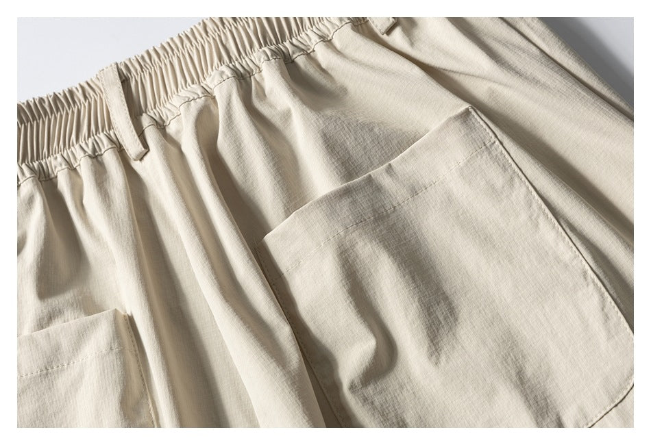 Close-up of light beige trousers showing an elastic waistband, belt loop, and large patch pockets.