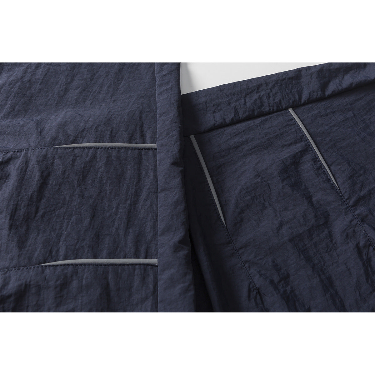 Close-up of navy garment panels with thin reflective piping and a pocket opening.