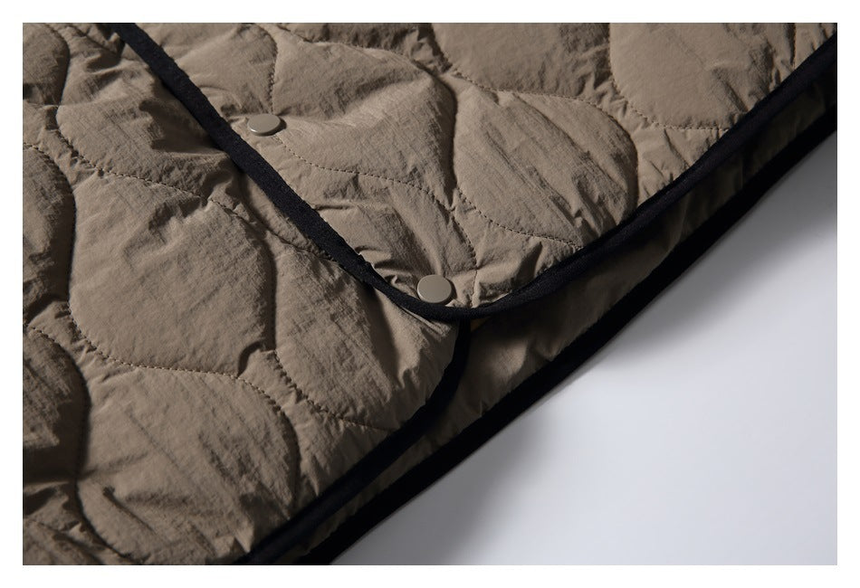 Close-up of the jacket's black-bound edge and two snap buttons against taupe quilted fabric.