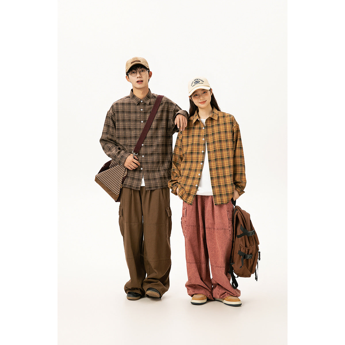 Two models wearing oversized brown and mustard plaid shirts with loose cargo pants against a white studio backdrop.