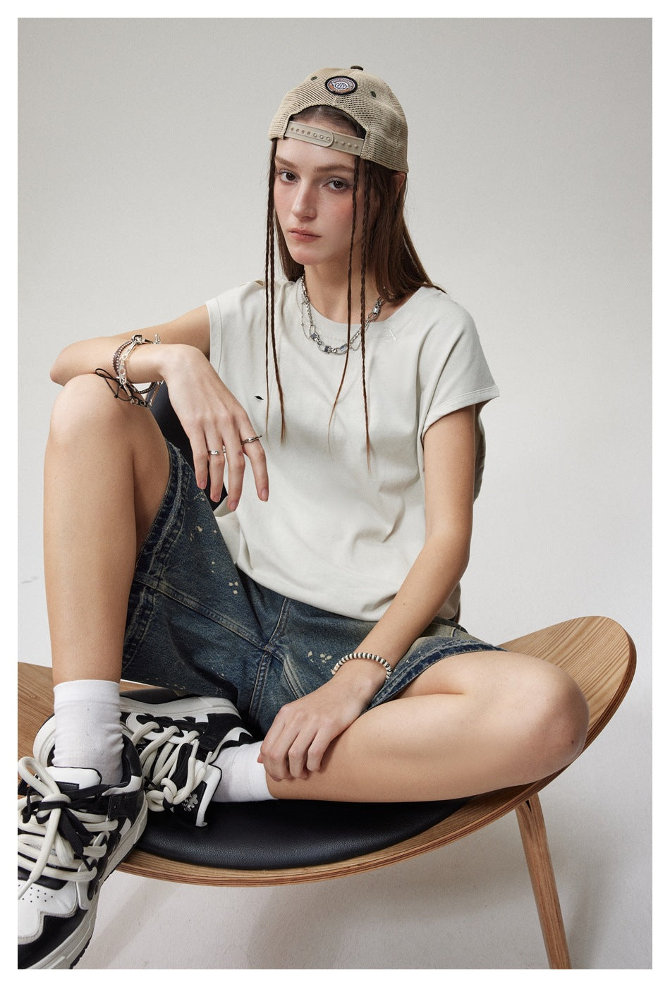 Seated model wearing a loose white cap-sleeve T-shirt with small distressed slits, shown from the front.