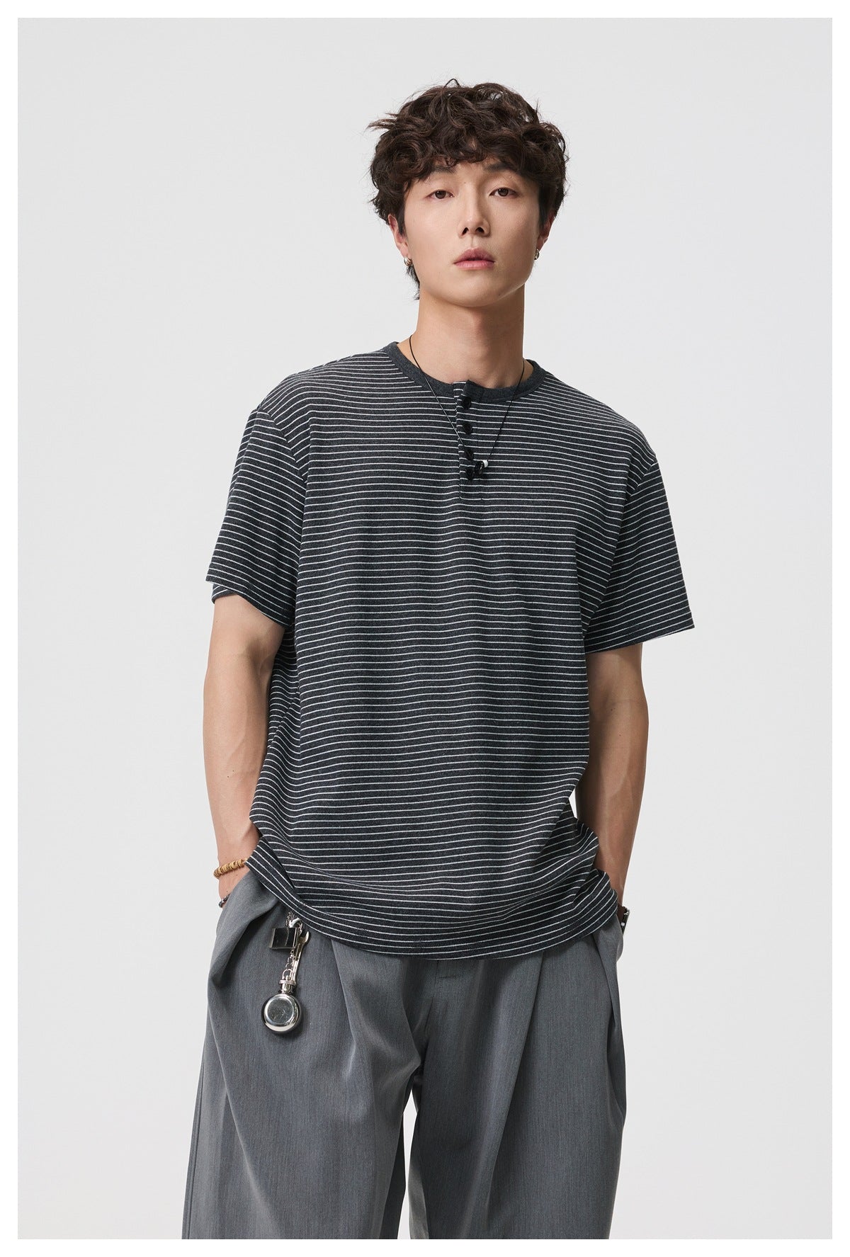 Man wearing a dark gray striped short-sleeve Henley T-shirt with gray pleated trousers, front view