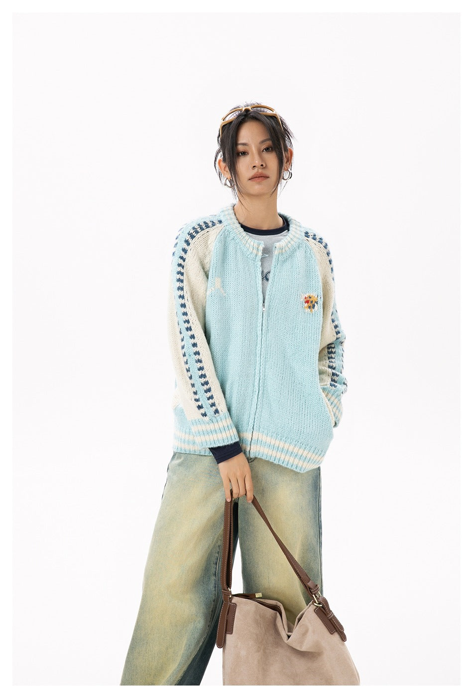 Front view of a model wearing a pale blue cardigan with cream patterned sleeves, striped ribbing, and a zip closure.