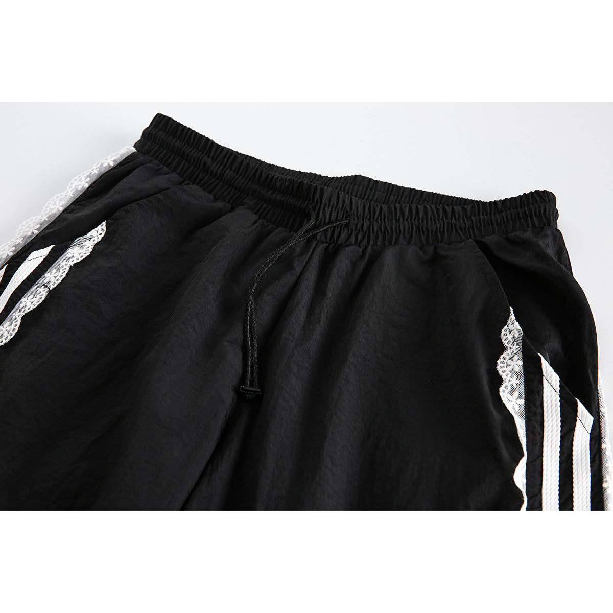 Close-up of black pants with an elastic drawstring waist and white striped, floral-lace side trim.