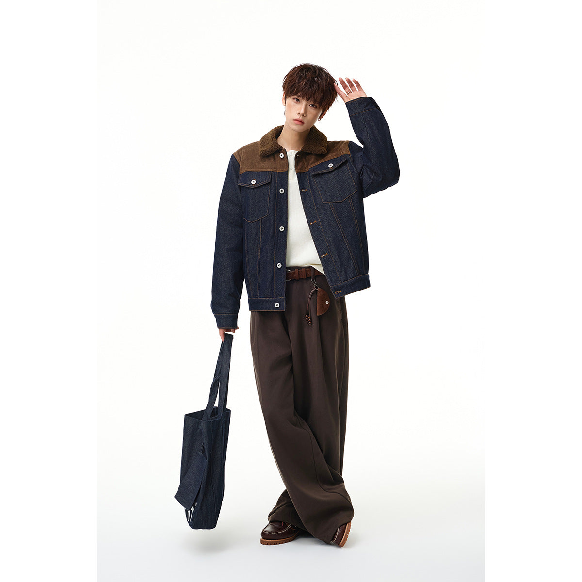 Model wearing a dark indigo denim jacket with brown shoulder panels and a sherpa collar, paired with wide dark trousers.