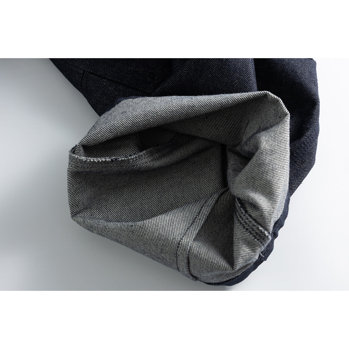 Close-up of a turned-up jeans cuff showing the dark outer denim and gray striped reverse side.