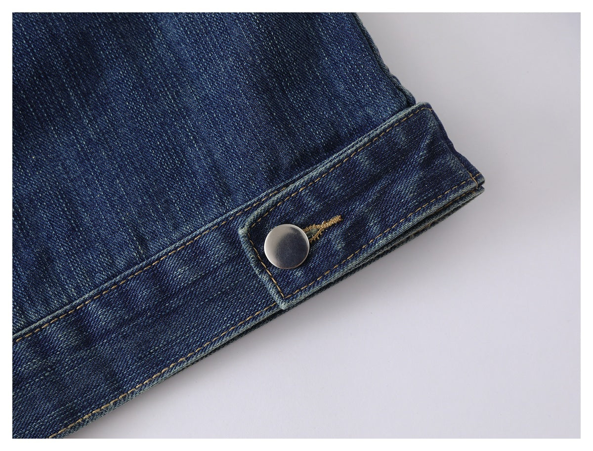 Close-up of a dark blue denim cuff with contrast stitching and a metal button tab.