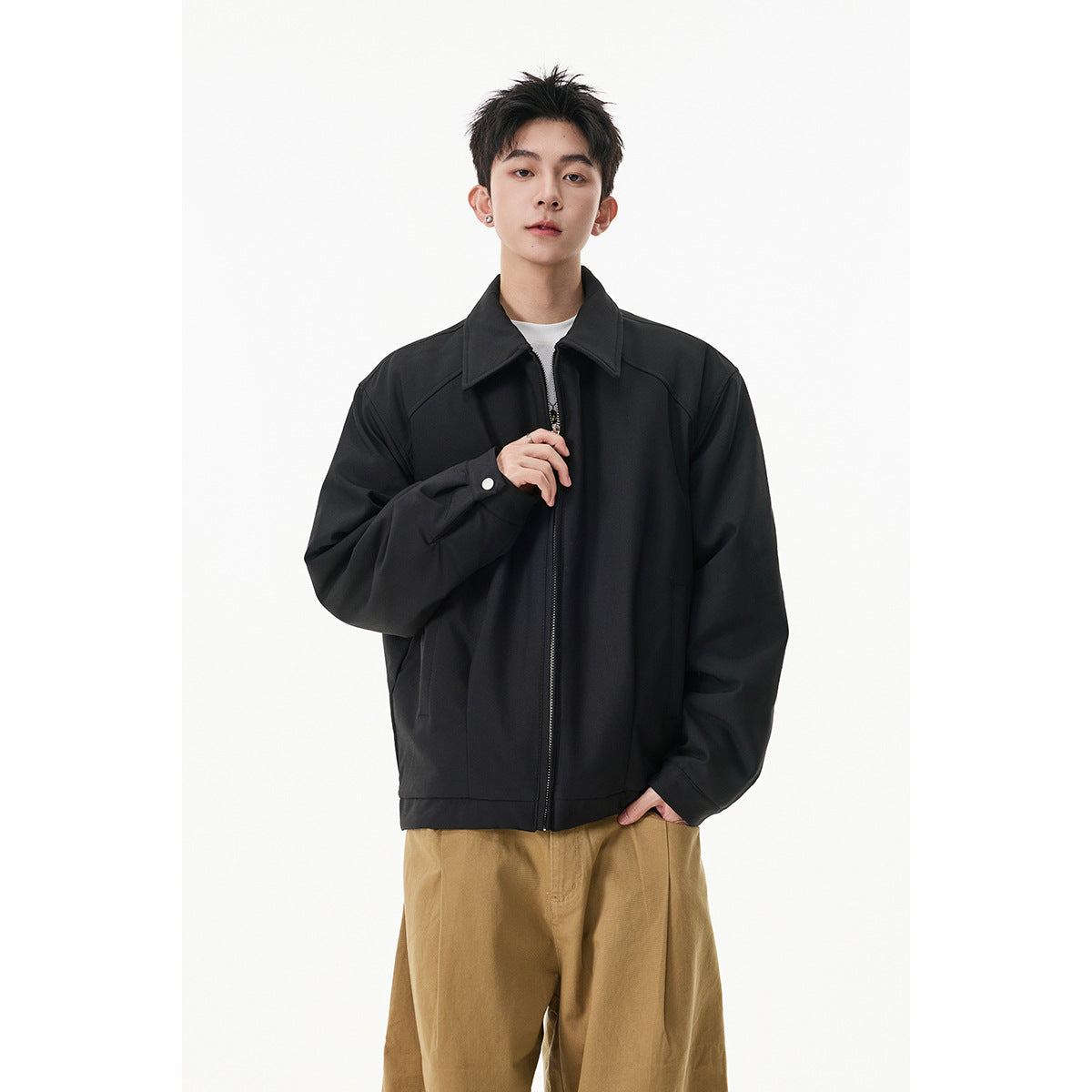 Model wearing a black collared zip jacket fastened at the front with loose tan trousers.