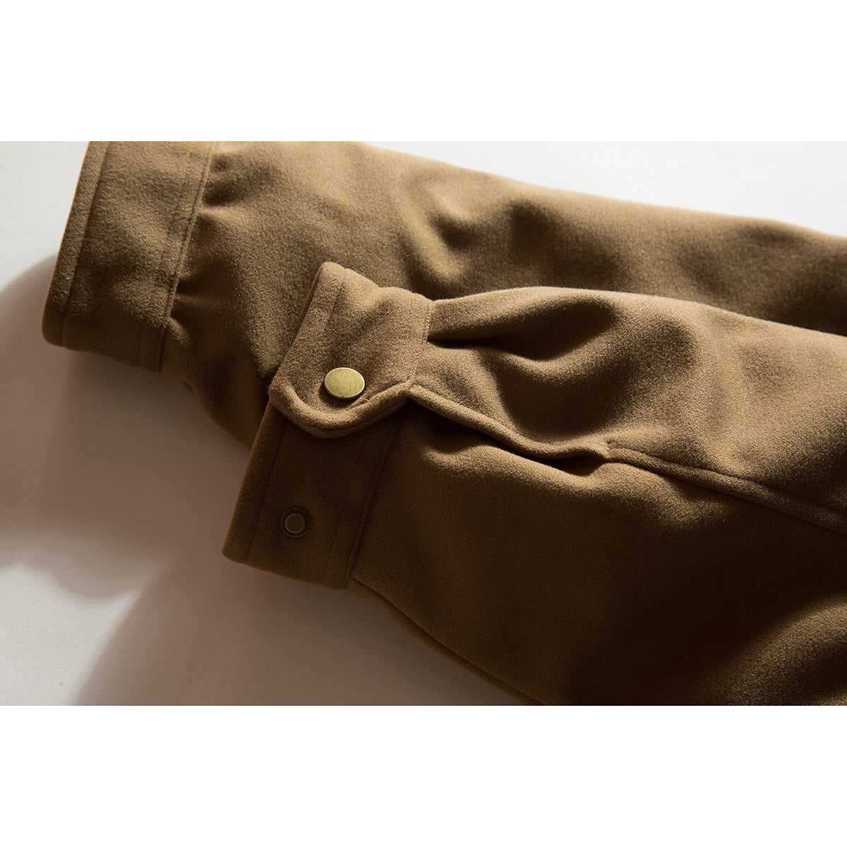 Close-up of a camel-brown coat sleeve cuff with a buttoned tab and brass-tone snap.