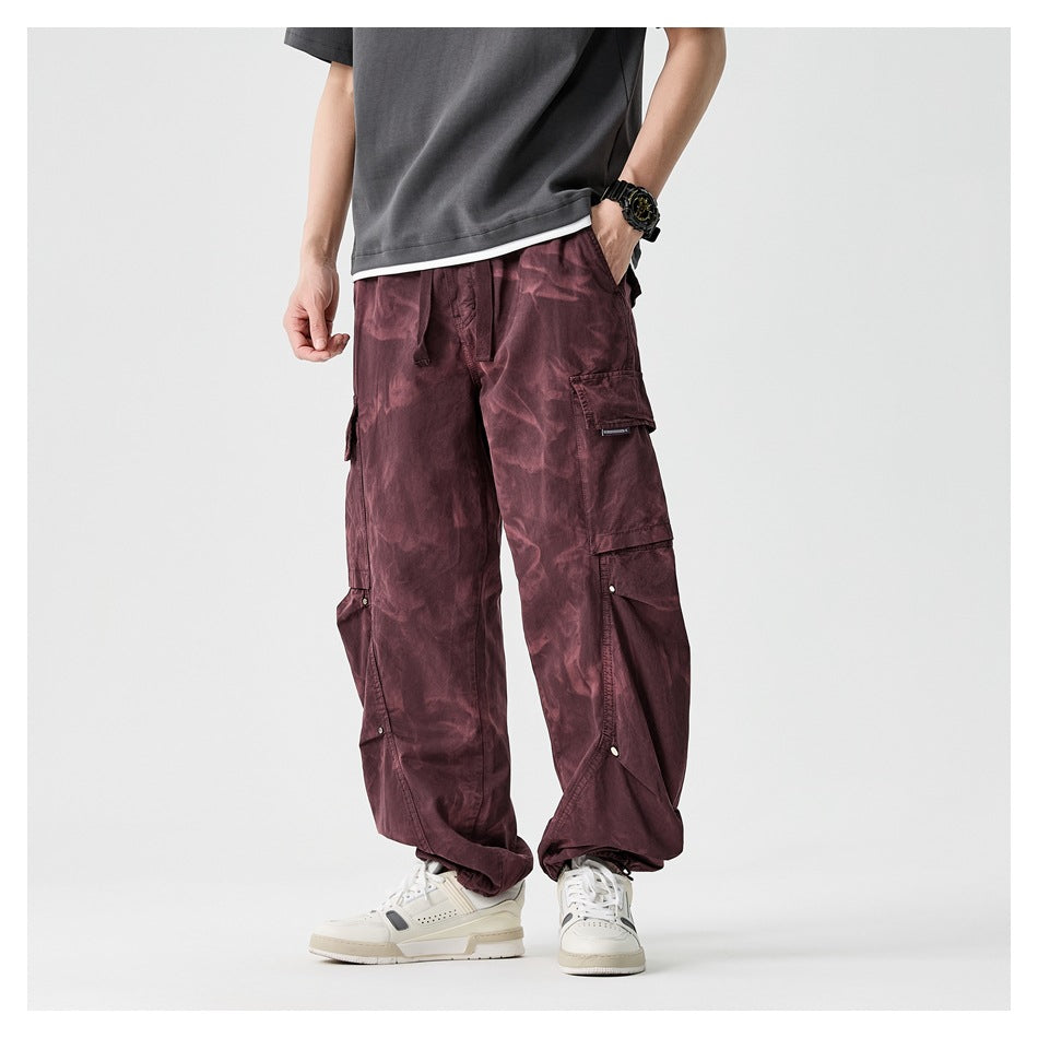 Front view of a model wearing loose burgundy cargo pants with multiple flap pockets and gathered ankle cuffs.