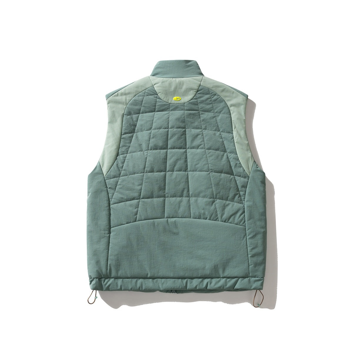 Back of a sage green quilted vest with pale green shoulder panels, a raised collar, and adjustable hem cords.