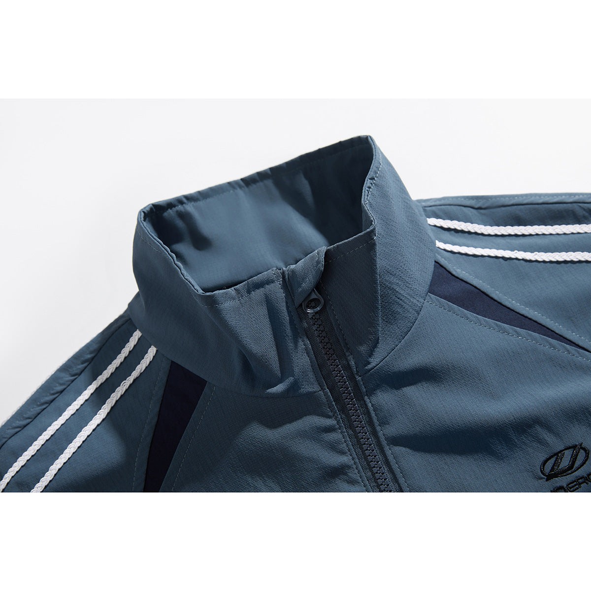 Close-up of a slate-blue track jacket's stand collar, front zipper and white braided shoulder stripes.