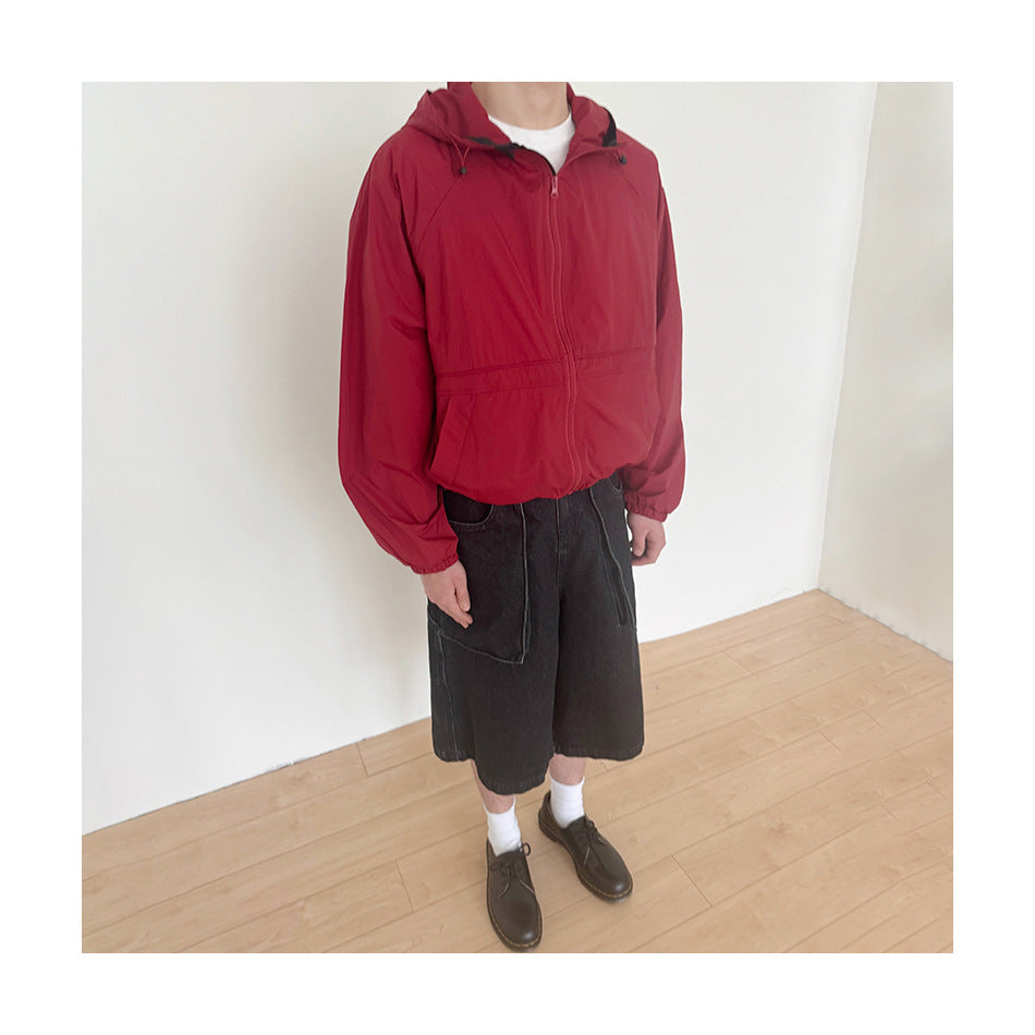 Person wearing a red hooded zip jacket with black shorts, shown from the neck down.